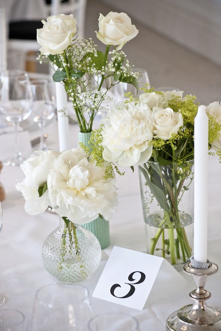 white flowers in vases on a table with candles and place cards for guests to sit at