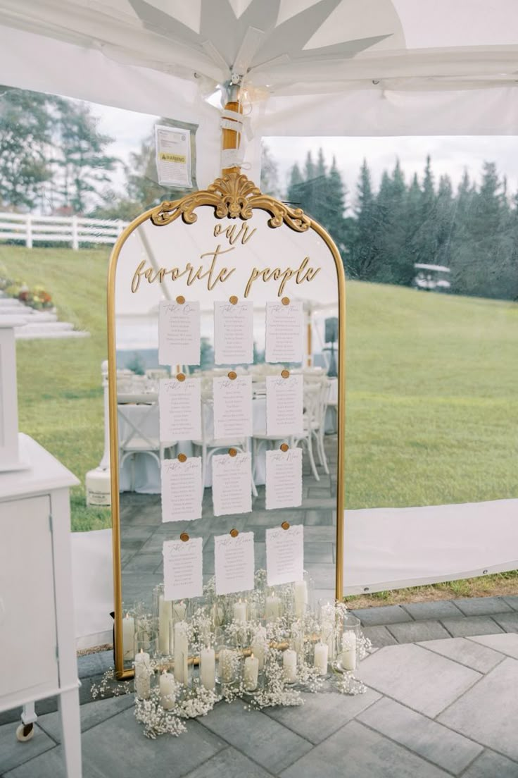 a table with seating cards and candles on it under a white tent at a wedding