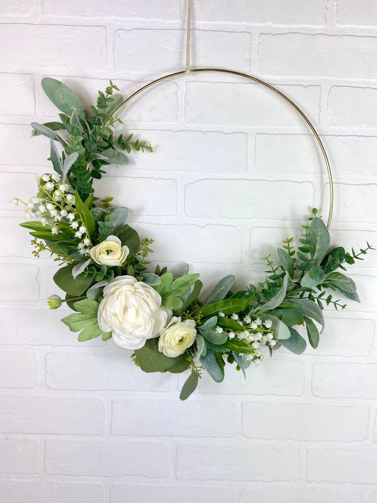 a wreath with white flowers and greenery hanging on a brick wall in front of a round metal frame