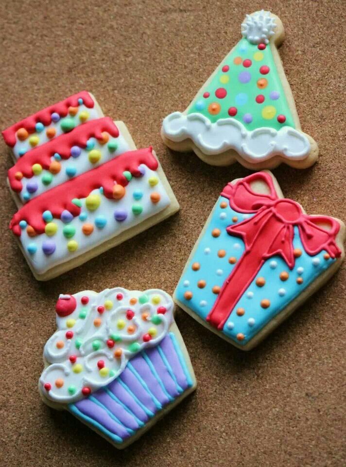 four decorated cookies sitting on top of a brown table next to a cupcake and cake