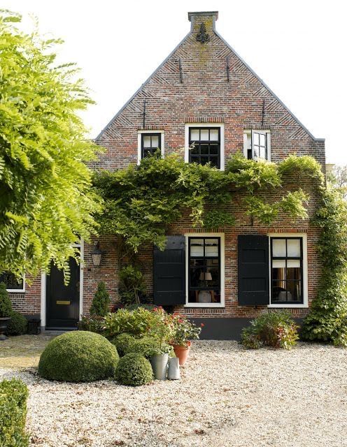 an old brick house with black shutters and ivy growing on the front door, surrounded by potted plants