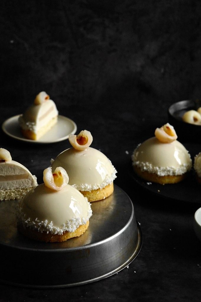 some desserts are sitting on black plates and one is white with icing in the middle