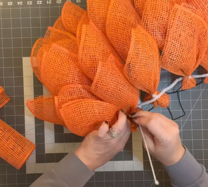 someone is working on an orange wreath made out of burlock and twine