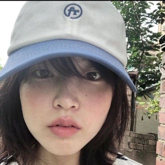 a young woman wearing a hat standing in front of a brick wall