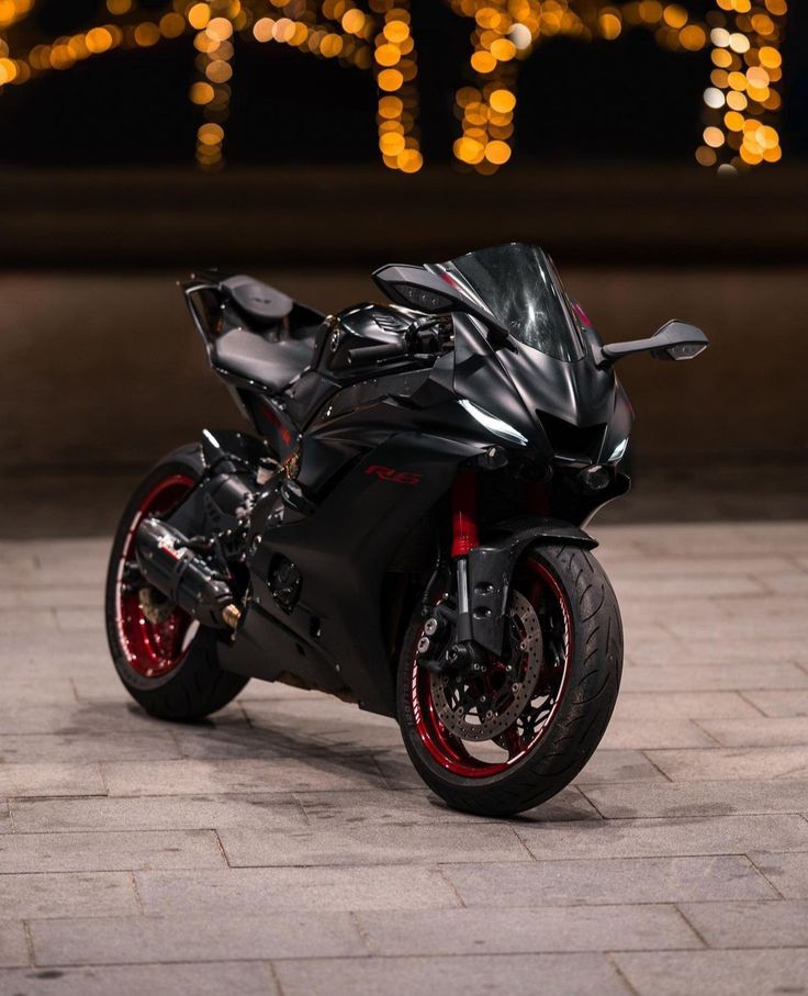 a black motorcycle parked on top of a brick floor next to a building with lights in the background