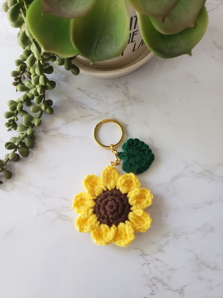 a crocheted sunflower keychain sitting on a table next to a potted plant