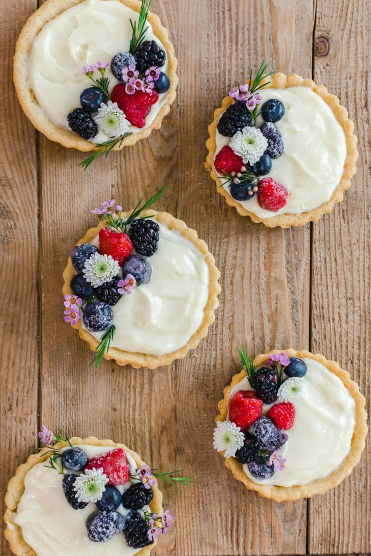 four small pies topped with fresh fruit on top of a wooden table