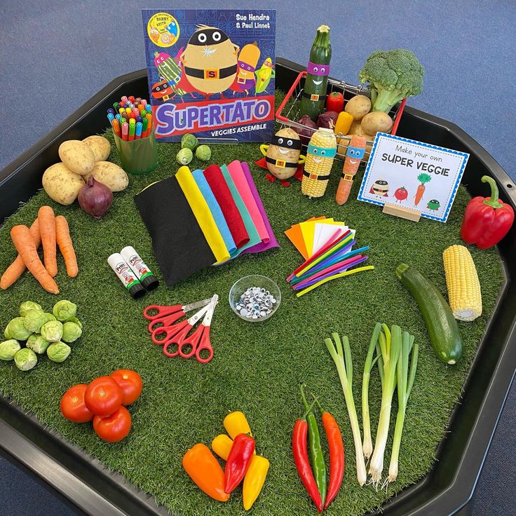 a tray filled with vegetables and fruit on top of a green grass covered floor next to a book