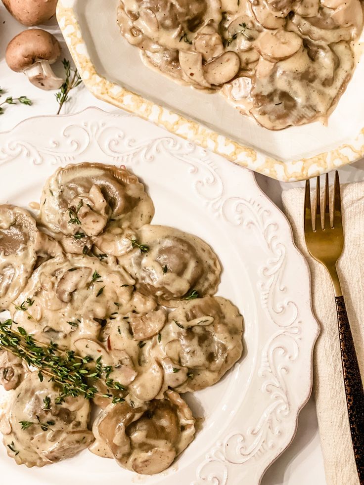 a white plate topped with ravioli covered in mushroom gravy next to mushrooms