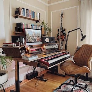 a living room filled with furniture and a computer desk covered in musical equipment next to a window