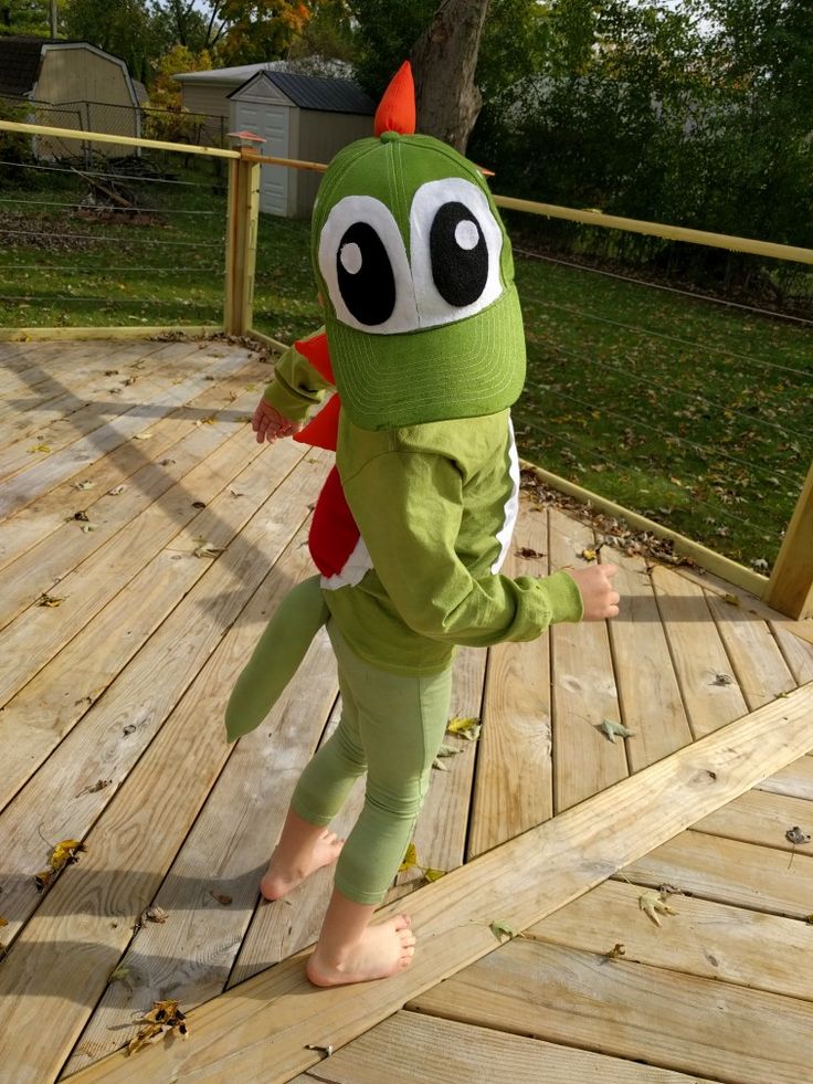 a young child in a green costume walking on a wooden deck with a red and white stuffed animal