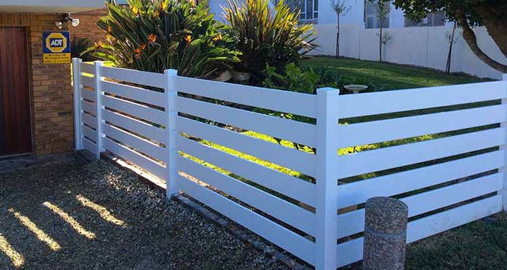 a white fence in front of a house with plants growing out of the top part