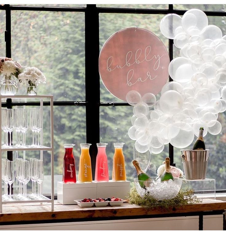 a table topped with lots of bottles and glasses next to a window filled with balloons