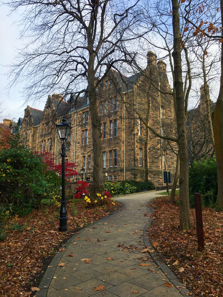 an old stone building in the fall with leaves on the ground and trees around it