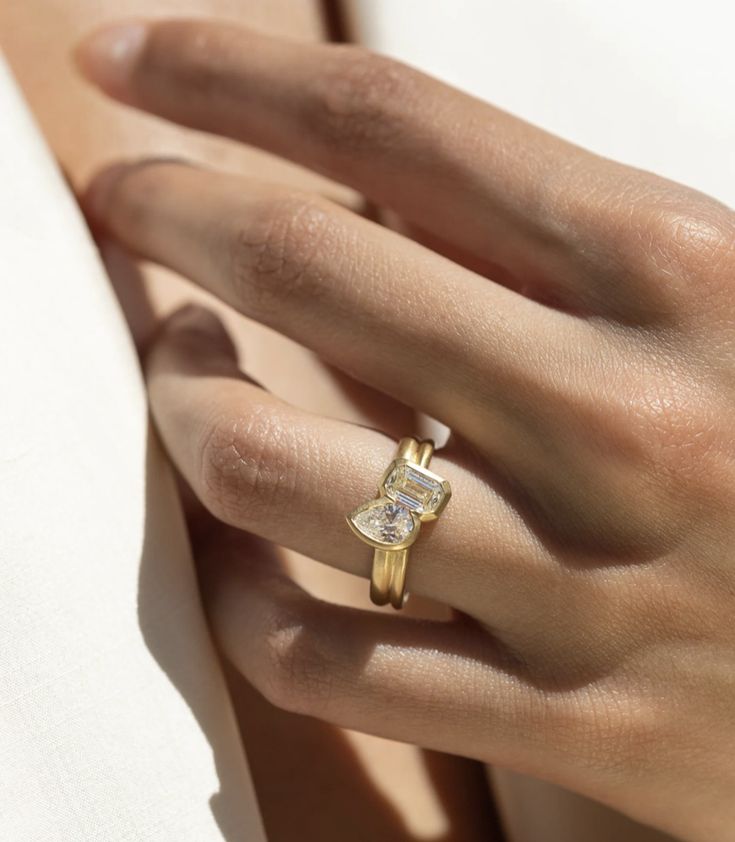 a woman's hand wearing a yellow gold ring with a square shaped diamond on it