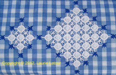 a blue and white checkered pillow with an embroidered design on the front, along with lacework