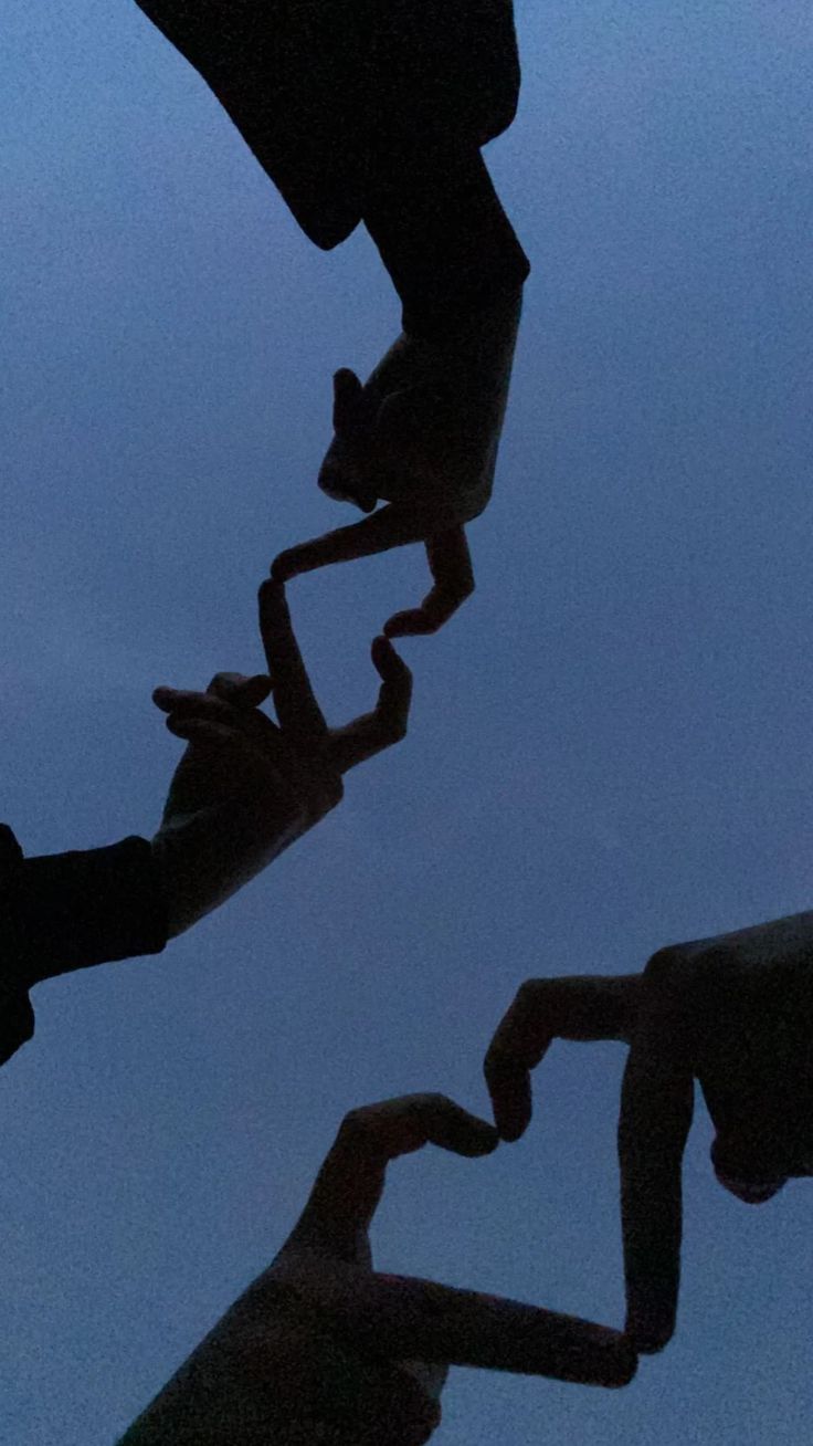 the silhouettes of two people holding hands in front of a blue sky