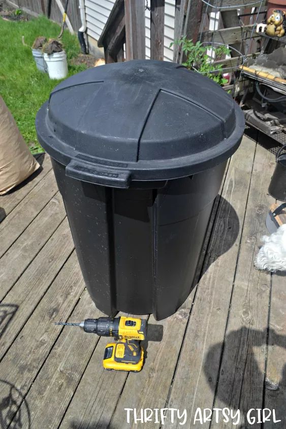 a black trash can sitting on top of a wooden deck next to a power drill