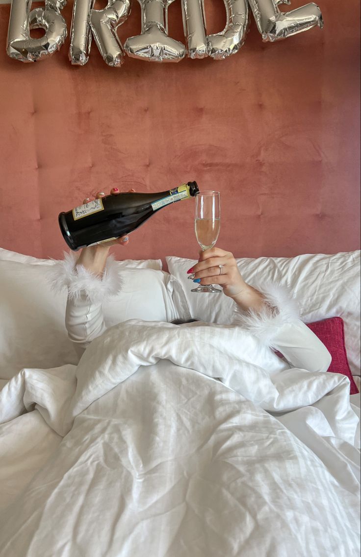 a woman laying in bed with a bottle of champagne and two balloons above her head