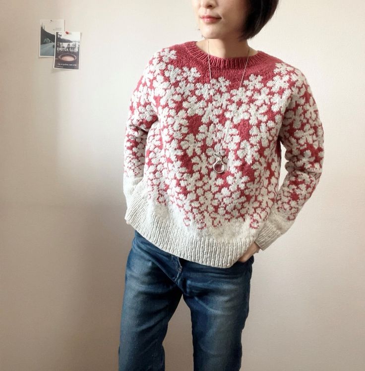 a woman standing in front of a white wall wearing a red and white flowered sweater