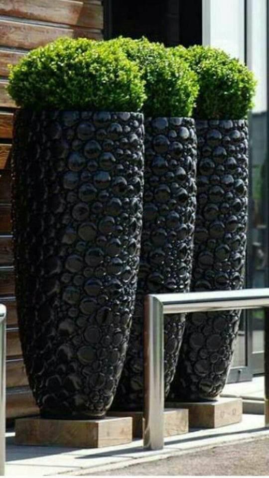 three large black vases with plants in them sitting on the side of a building