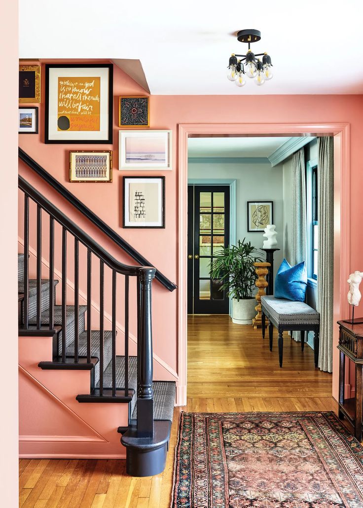 a living room with pink walls and pictures on the wall next to stairs leading up to an entryway