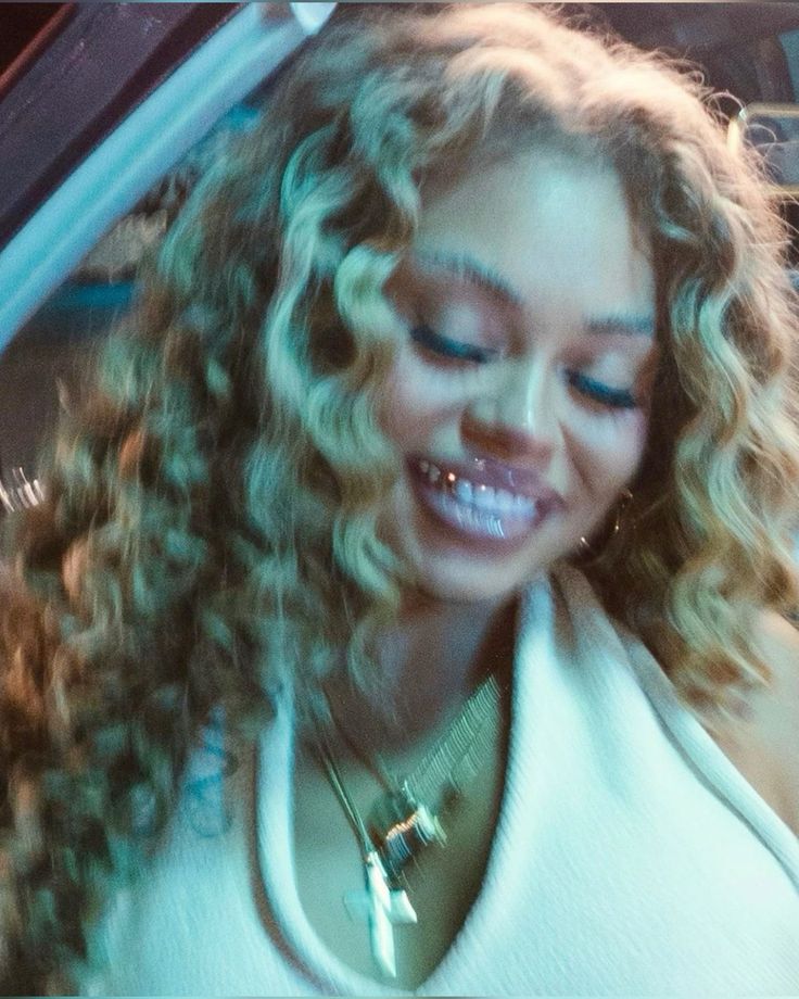 a woman with curly hair is smiling and looking at her cell phone while sitting in the back seat of a car