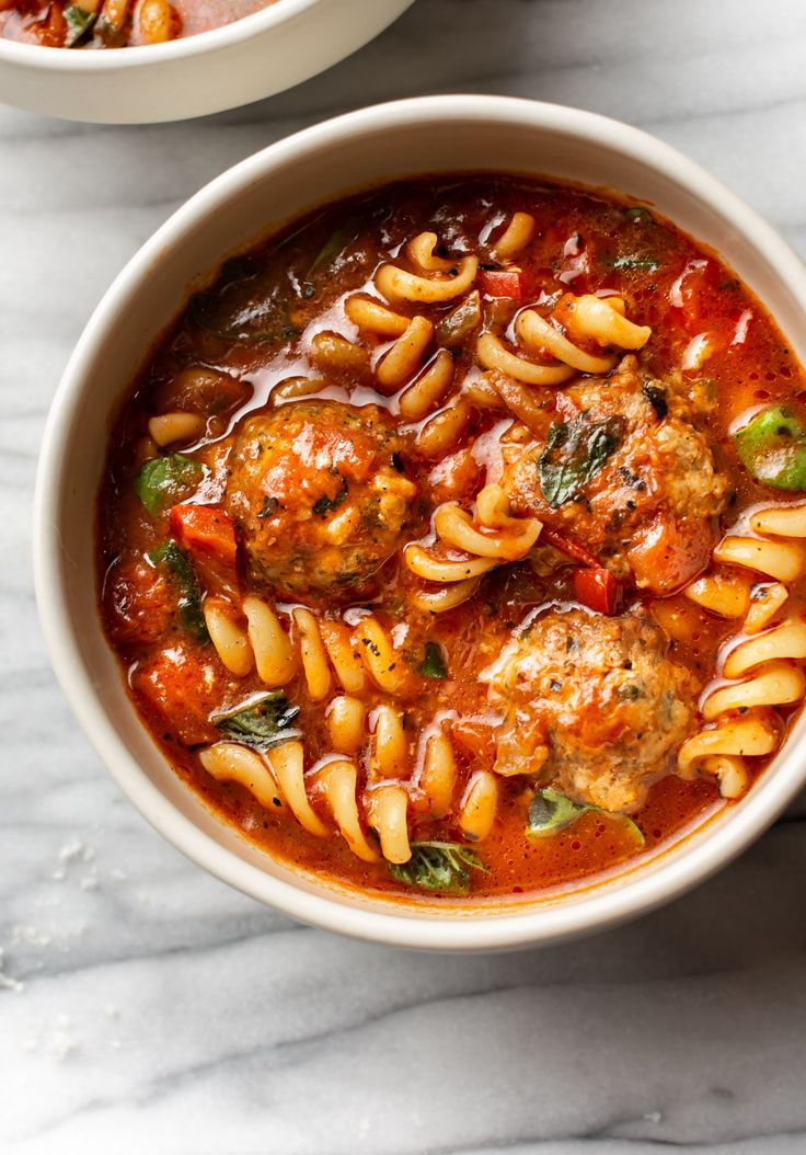 two bowls filled with pasta and meatballs on top of a white table next to another bowl