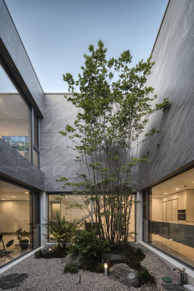 an indoor courtyard with trees and rocks in the foreground, surrounded by glass windows