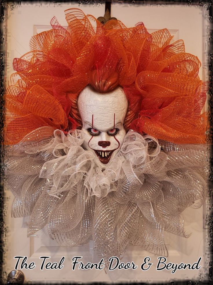 a creepy clown with red hair and makeup on his face is hanging from a door