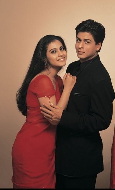 two people standing next to each other in front of a white wall and one person wearing a red dress