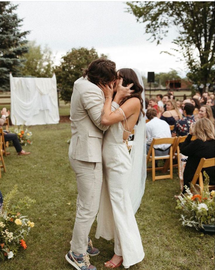 two people are kissing each other in front of an outdoor wedding ceremony with flowers on the grass