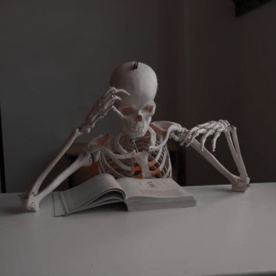 a skeleton sitting at a table reading a book