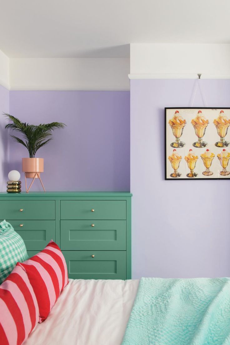 a bedroom with purple walls, green dressers and pink striped pillows on the bed