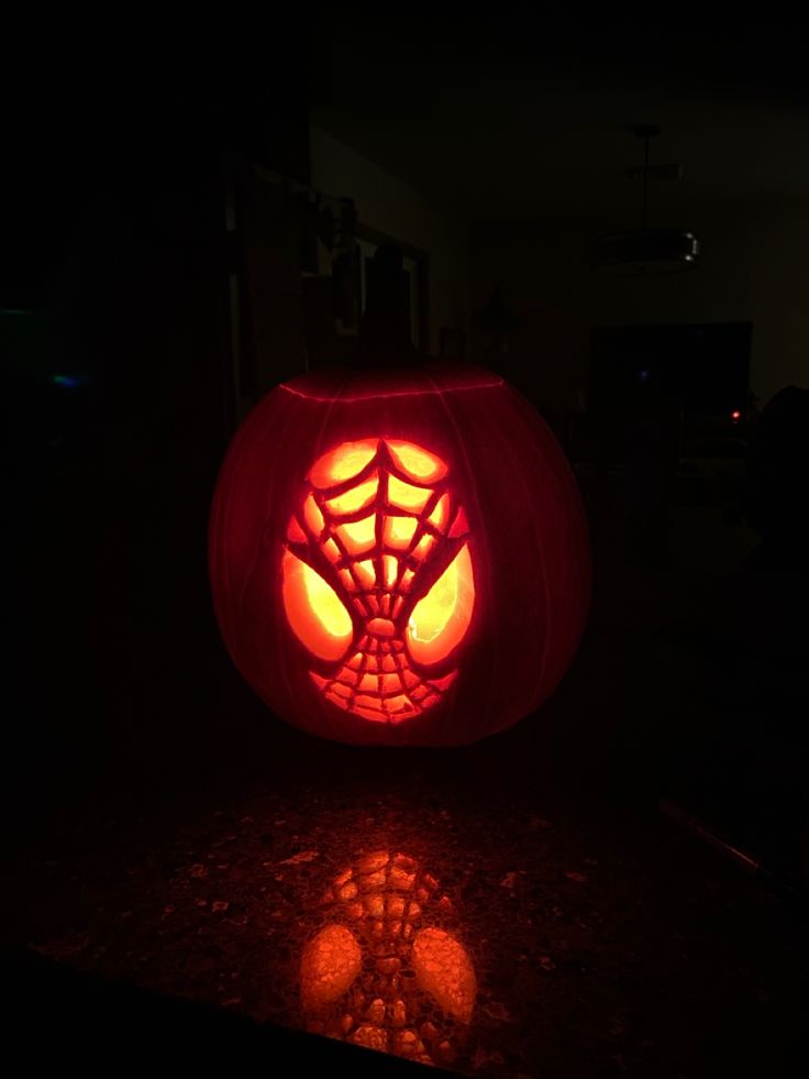 a pumpkin carved to look like a spiderman's web in the dark with its eyes glowing