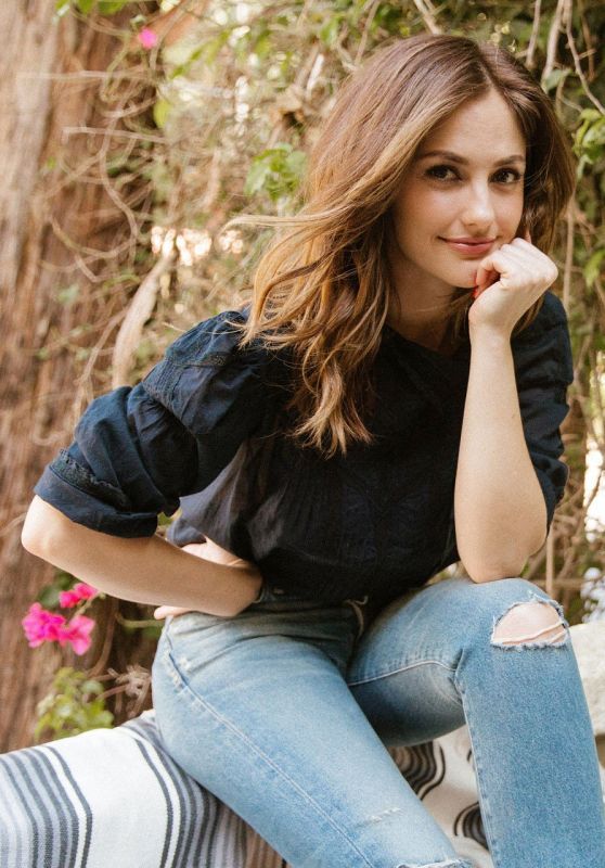 a beautiful young woman sitting on top of a wooden bench in front of some trees