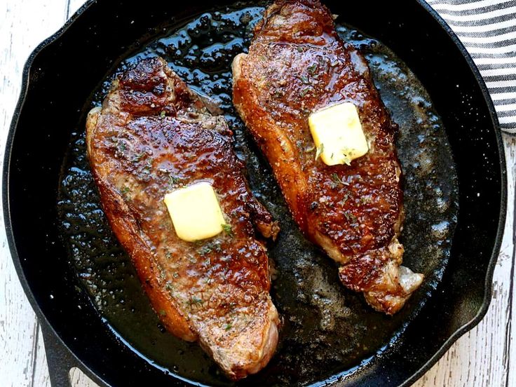 two steaks in a skillet with butter on top