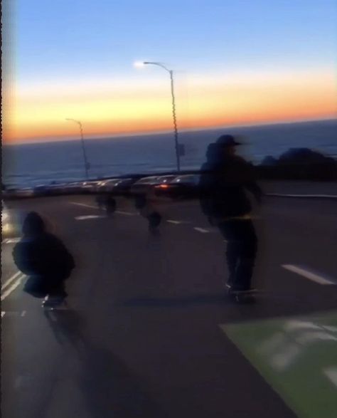 blurry image of people skateboarding on the road at sunset or dawn with an ocean in the background