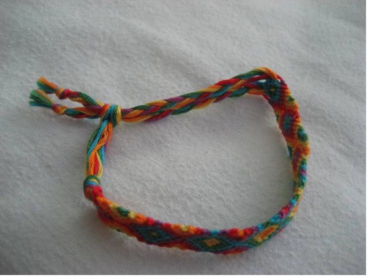 a multicolored rope bracelet on a white sheet with the string attached to it