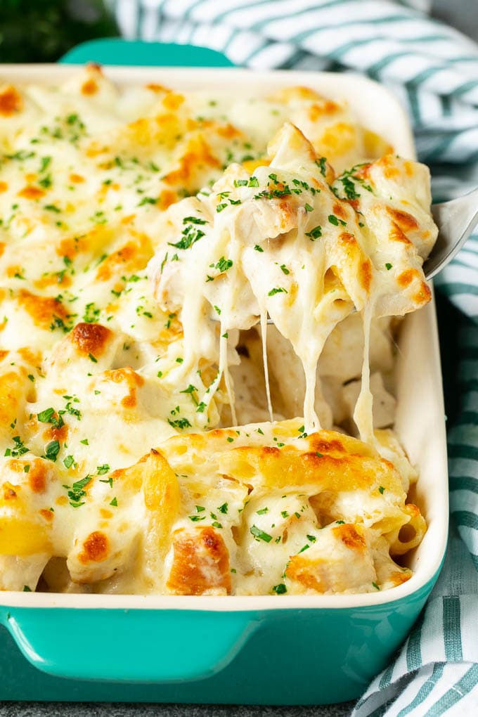 a casserole dish with chicken and cheese being lifted from the casserole