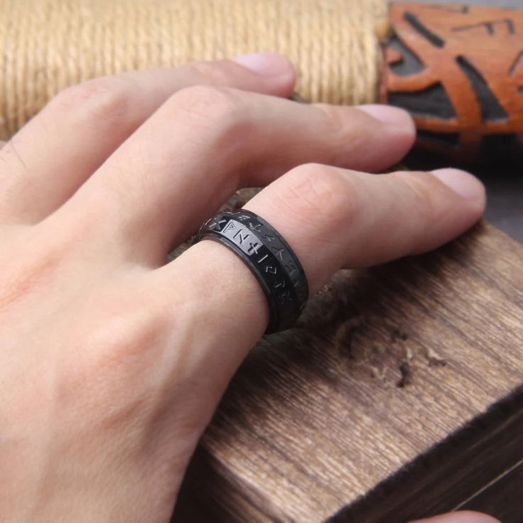 a person wearing a black ring with roman numerals on it and a wooden object in the background