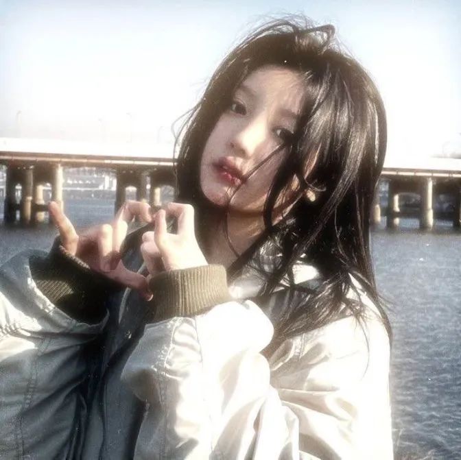 a woman standing in front of the water with her fingers up