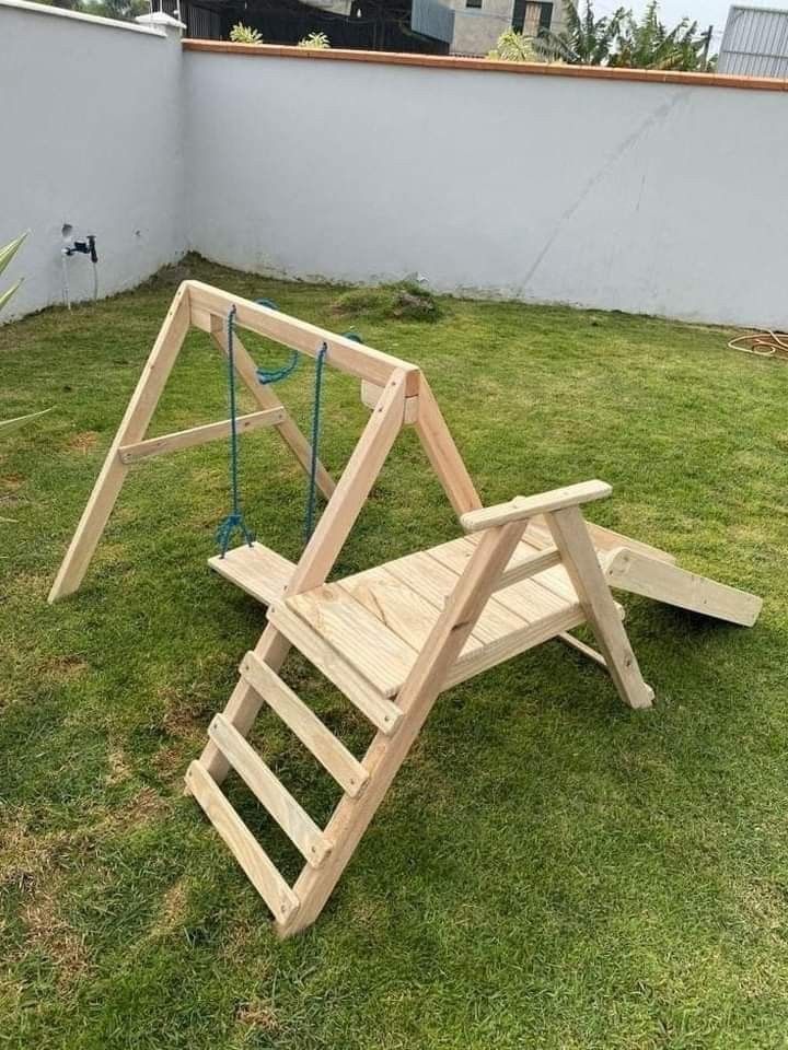 a wooden swing set sitting on top of a green grass covered field next to a white wall