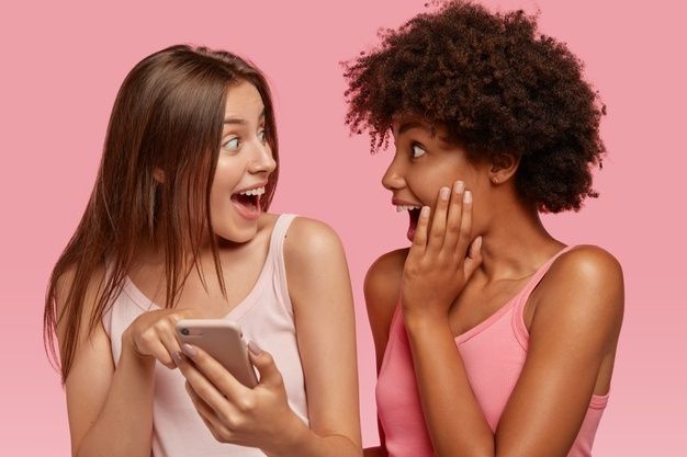 two young women laughing and looking at a cell phone