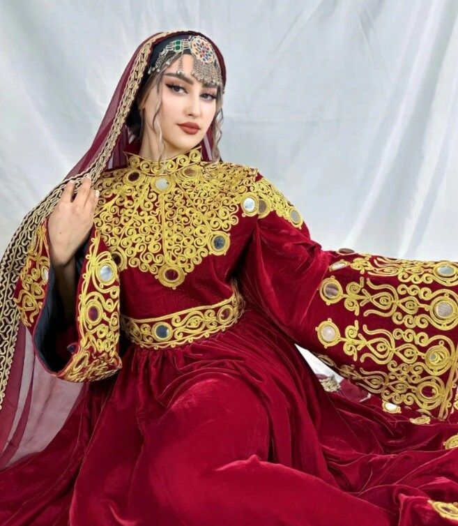 a woman in a red and gold dress sitting on a white surface with her hands behind her head