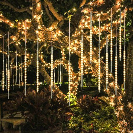 an outdoor string light display with white lights hanging from it's branches in front of a tree