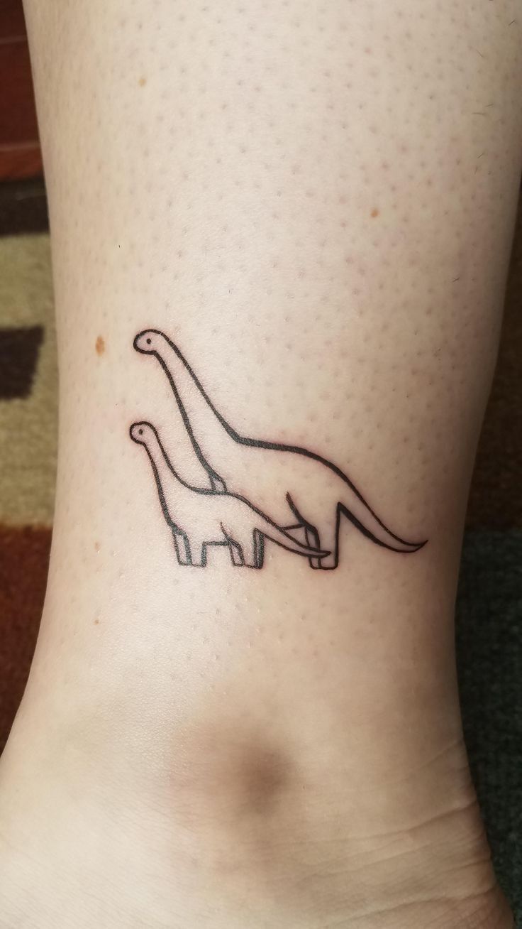 a small tattoo on the ankle of a woman's foot, depicting two dinosaurs