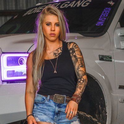 a beautiful young woman sitting on the hood of a white truck in front of a purple light