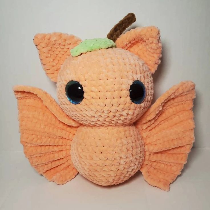 an orange stuffed animal with big eyes and a green bow on its head, sitting against a white background