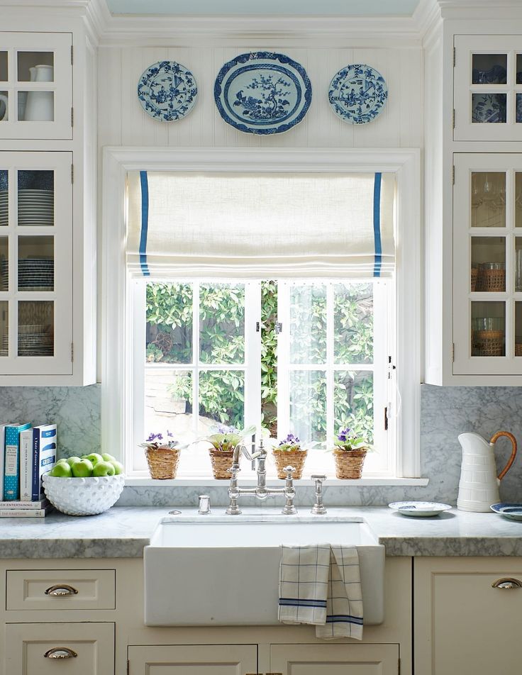 a white kitchen with blue and white dishes on the window sill above the sink